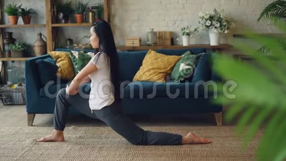 亚洲女体操运动员在家训练练习在客厅里坐在地毯上劈腿积极的生活方式视频的预览图