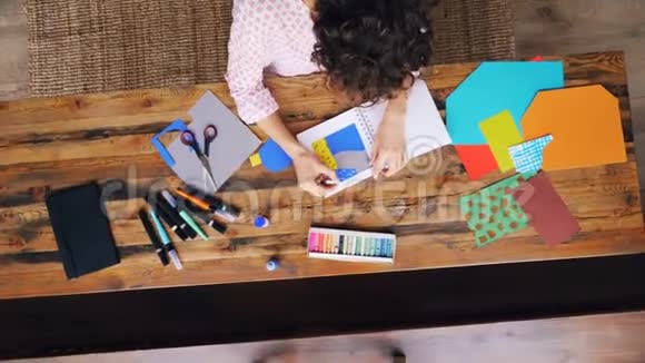 女员工创意设计师用蜡笔在笔记本上的彩色纸拼贴画进行缩放视频的预览图