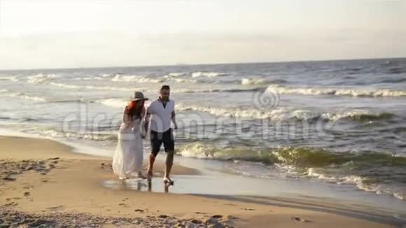 沙滩上恋爱的年轻夫妇穿着白色衣服的漂亮夫妇情人牵手拥抱视频的预览图