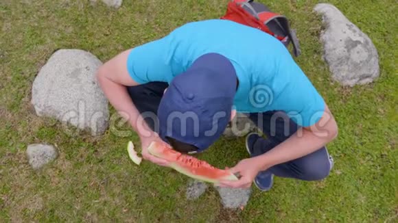 男人吃一片香甜多汁的西瓜在户外微笑高角度观看视频的预览图