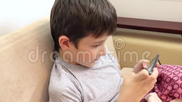 一个男孩坐在沙发上在智能手机上玩游戏视频的预览图