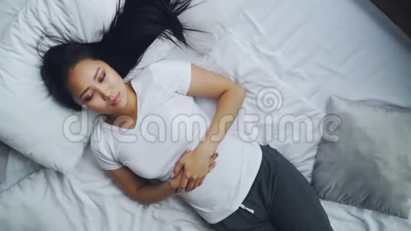 漂亮的亚洲女士睡在床上然后睁开眼睛微笑着伸展手臂柔软的枕头和白色亚麻布视频的预览图