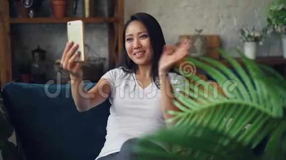微笑的亚洲女学生正在打在线视频电话看着智能手机屏幕有说有笑地坐着视频的预览图