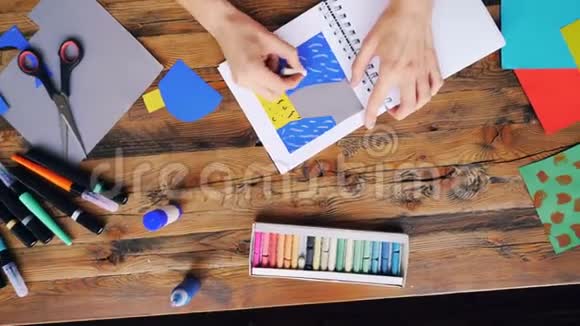 用蜡笔在家庭办公室的办公桌上做纸拼贴画的创意深色头发艺术家视频的预览图