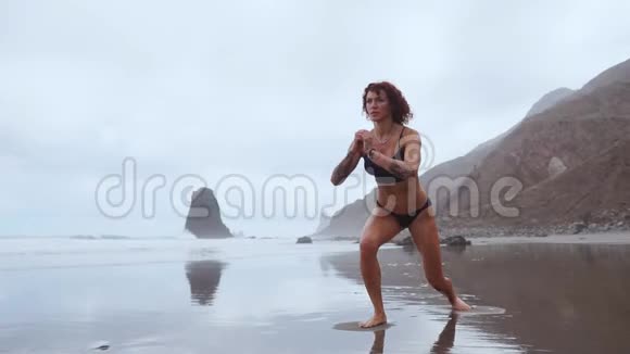 一位身材苗条的女士在海洋附近散步在水上运动在每条腿上表演弓步大腿肌肉锻炼视频的预览图