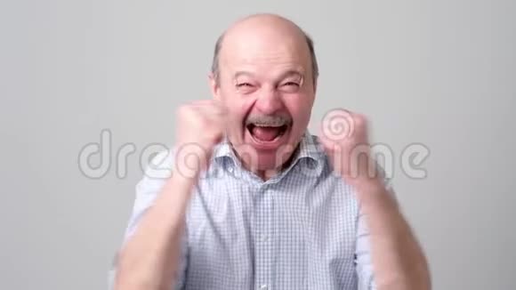 快乐的秃顶老人穿着衬衫庆祝他在灰色背景下的成功视频的预览图