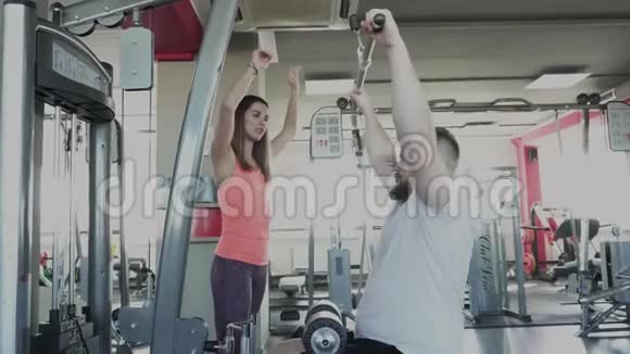 男人在健身房的训练模拟器上与私人教练摆动手臂肌肉个人减肥训练视频的预览图