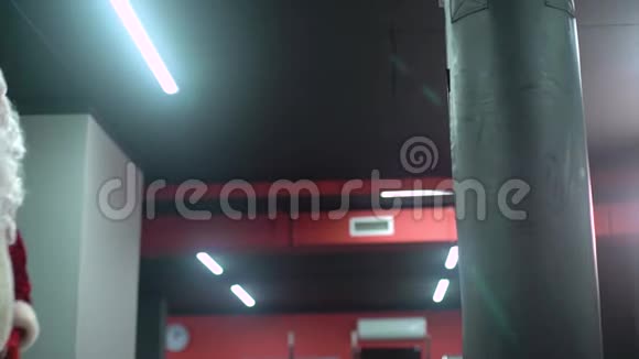 圣克劳斯拳击手与红色绷带拳击手击打一个巨大的拳击袋在拳击工作室圣诞老人拳击手视频的预览图