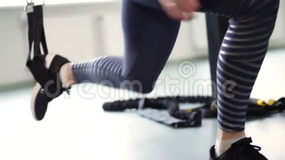 特写女腿穿腿裤和运动鞋女人在TRX循环上做运动陷阱参加运动视频的预览图
