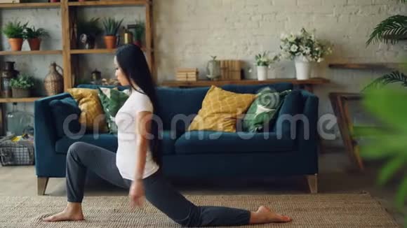 苗条的亚洲女运动员正在家中练习分腿坐在地板上然后在个人练习中向前弯曲视频的预览图