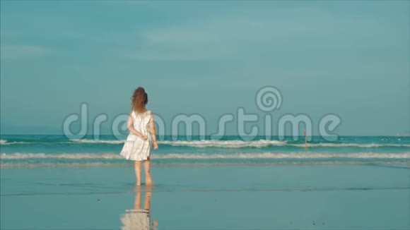 卷曲的小女孩穿着白色连衣裙在日落时在海滩上散步动作缓慢快乐的童年自由和旅行视频的预览图