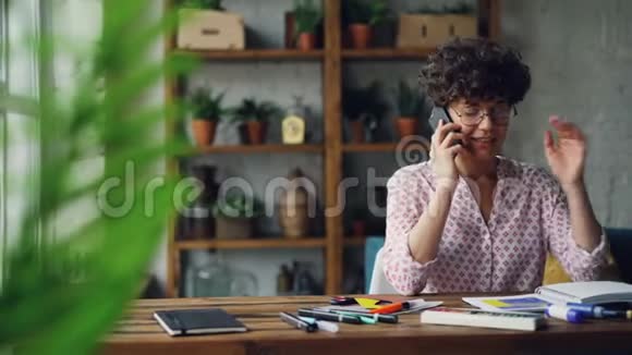 漂亮的女设计师正在智能手机上聊天坐在桌子旁触摸在家工作的文具现代视频的预览图