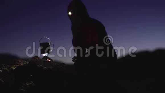 一个头上拿着手电筒的女孩在山上结冰在山上烧水用燃气燃烧器温暖她的手视频的预览图