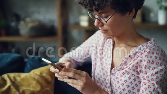 戴着眼镜和休闲服装的漂亮黑发女人正在触摸智能手机屏幕然后手里拿着手机说话视频的预览图