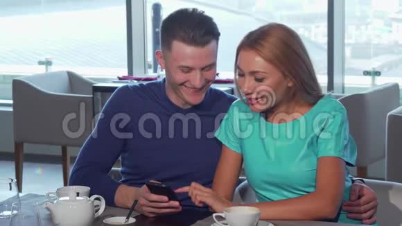 幸福的爱人拥抱在一起在咖啡馆里用智能手机视频的预览图