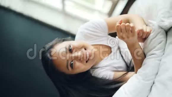 慢动作美丽的亚洲黑发女人在床上翻滚高兴地微笑着看着相机享受着乐趣视频的预览图