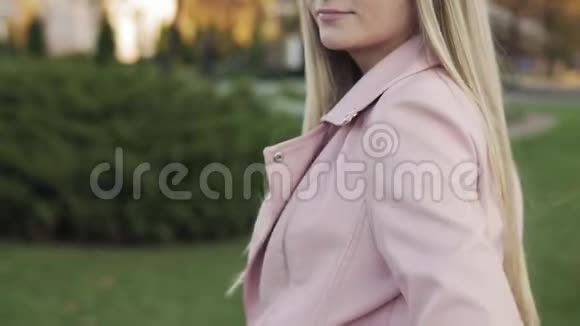 金发女人走在户外穿粉色夹克的女人慢动作视频的预览图