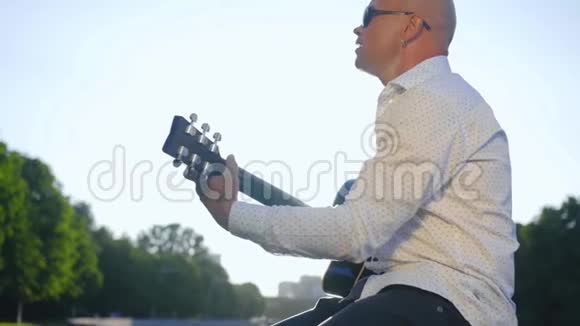 一个秃顶的人在公园里弹吉他唱歌吉他手触摸吉他弦中弹视频的预览图