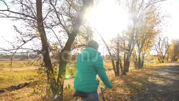 年轻女孩骑自行车在一条秋天的路上慢动作视频的预览图
