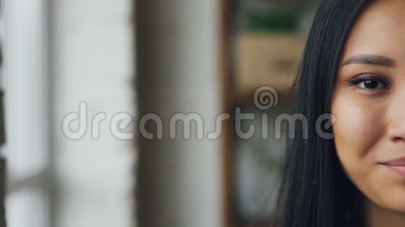 动作慢镜头亚洲女孩的特写镜头半张脸看着镜头在模糊的背景下微笑视频的预览图