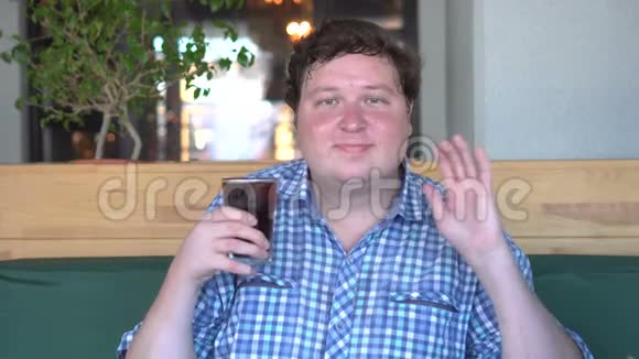 胖子在咖啡馆里拿着一杯饮料可乐挥手打招呼视频的预览图