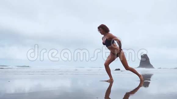 沿着海洋一个女人在岩石和岩石的背景下轮流在每一条腿上进行运动表演视频的预览图