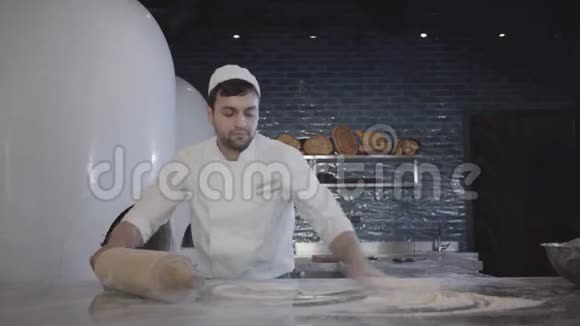 在现代餐厅厨师穿着白色制服用大木头面团擀面杖在桌子上快速擀面视频的预览图