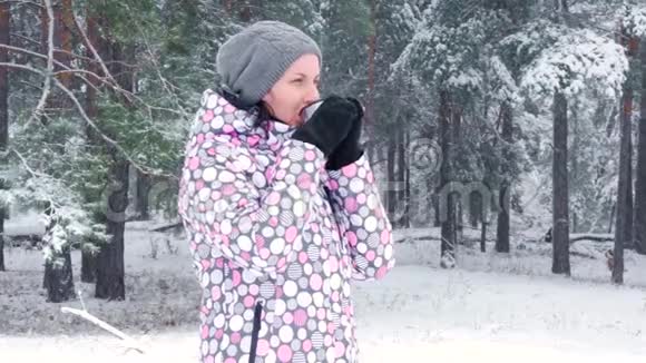 一个年轻的女游客在冬天的森林里喝热茶在降雪积极娱乐旅游的概念视频的预览图