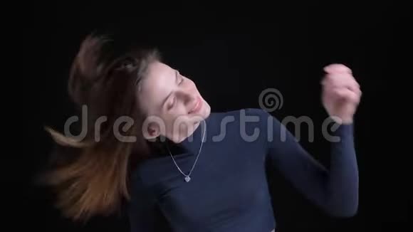 年轻苗条的白种人女孩在黑色背景下摇动头发和跳舞的肖像视频的预览图