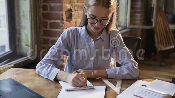 可爱的白种人学生女孩在笔记本上做笔记坐在红砖旁边的桌子旁学习和工作视频的预览图