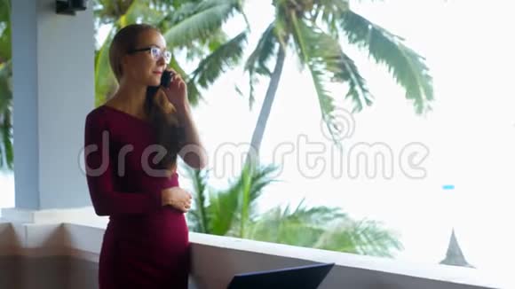 戴眼镜的金发女孩在棕榈树的阳台上打电话视频的预览图