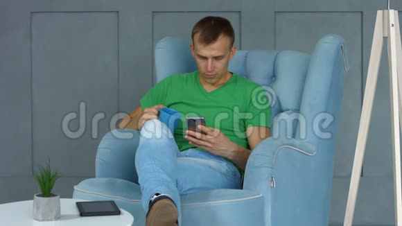有电话的帅哥坐在家里的扶手椅上视频的预览图