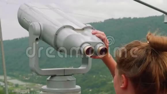 年轻的白种人金发女孩在观景台上用望远镜看山视频的预览图