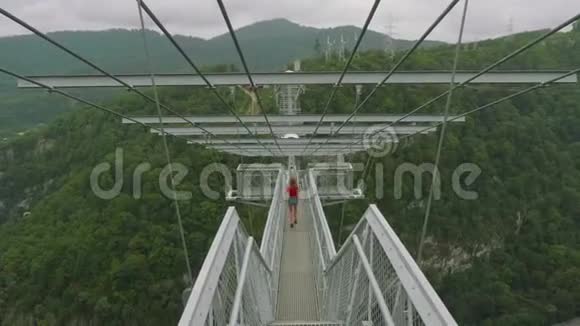 年轻的白种人金发碧眼的金发女郎正在从摄像机上的吊桥上奔跑在高处自拍视频的预览图