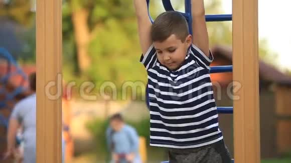 一个穿着条纹T恤的小男孩正在操场上玩在秋千上荡秋千春天晴朗的天气视频的预览图