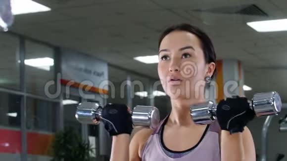 培训一个年轻的女人用哑铃抽她的手肌肉照镜子肖像视频的预览图