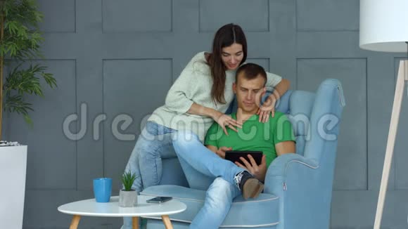 休闲情侣分享平板电脑坐在扶手椅上视频的预览图