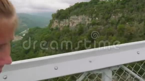 年轻的白种人金发碧眼的人走在高高的悬索桥上与河流相连视频的预览图