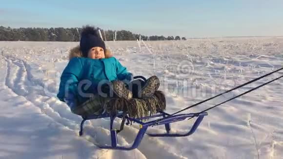 坐雪橇的小男孩宝贝在雪橇上孩子们在雪地里户外玩耍愉快的寒假冬季视频的预览图