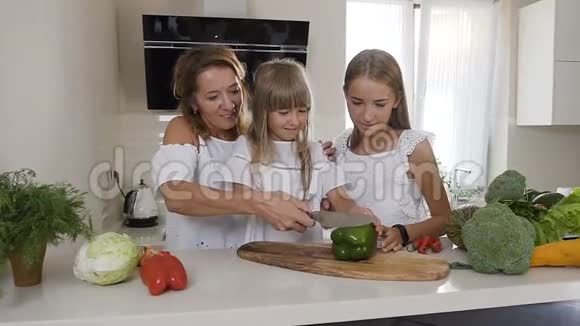 妈妈和她的两个女儿在厨房做饭女人切蔬菜青椒做沙拉教她视频的预览图