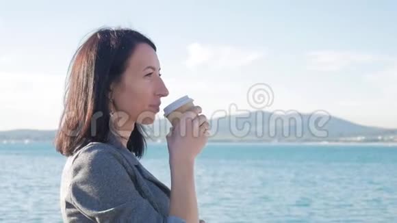年轻美丽的女孩在秋天寒冷的海洋里走来走去喝咖啡欧洲旅游目的地游客视频的预览图
