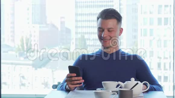 快乐地笑着的开朗英俊的男人用他的智能手机喝茶视频的预览图