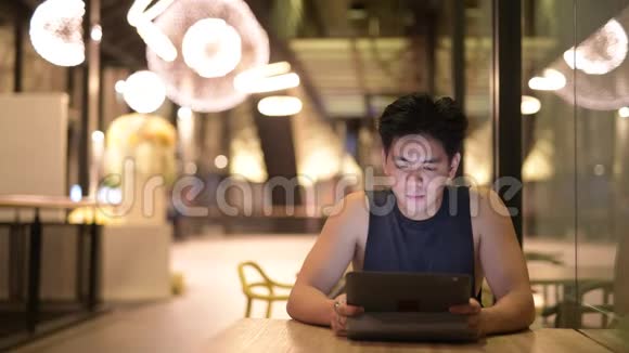 年轻快乐英俊的亚洲男人晚上在餐馆里用数码平板电脑视频的预览图