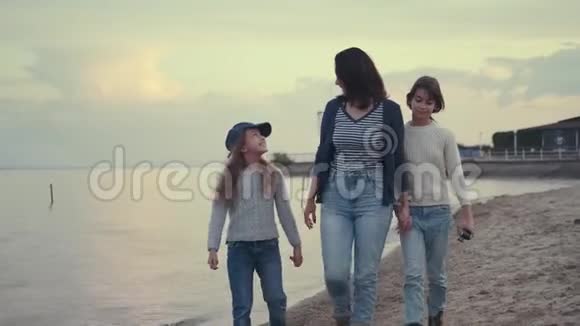 日落时年轻的母亲和她的孩子在海滨散步这个家庭花时间在户外视频的预览图