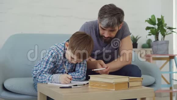 勤奋的小学生在作业本上写作业而他慈爱的父亲在帮助他教育视频的预览图