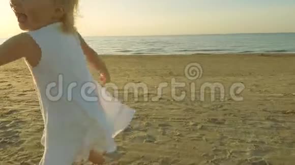 可爱的小女孩穿着白色裙子在沙滩上奔跑视频的预览图