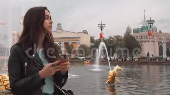 漂亮的时尚女孩在喷泉背景上打手机视频的预览图