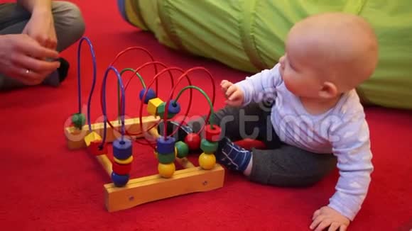 一岁的婴儿坐在地板上玩一个木制的玩具红色背景孩子的父亲是视频的预览图