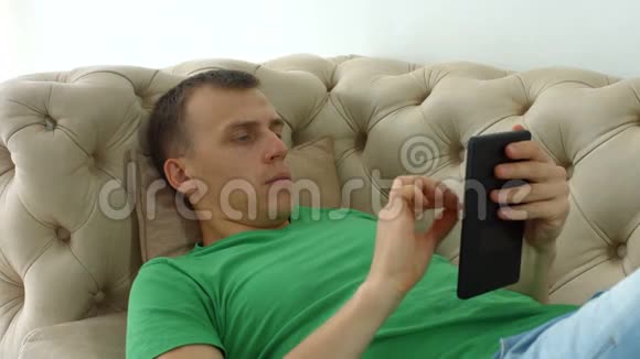 快乐的男人在沙发上用平板电脑上网视频的预览图