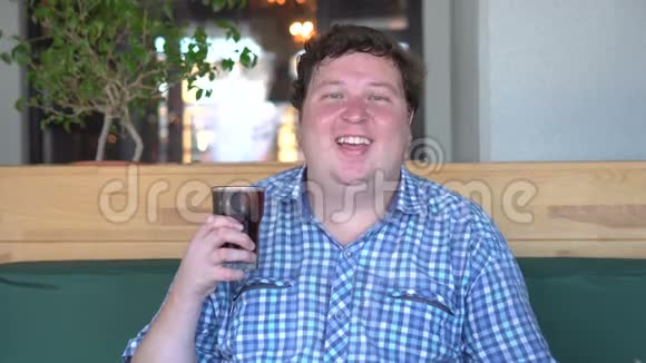 胖胖的快乐男人拿着一杯软饮料可乐笑着坐在咖啡馆里饮料视频的预览图